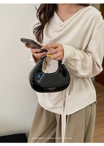 Détail du sac croissant en cuir verni noir avec boucles dorées et lettrage décoratif