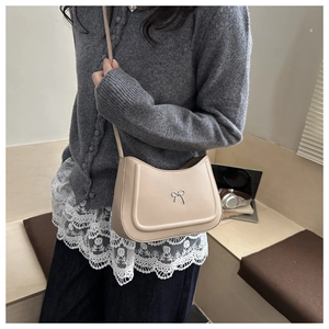 Detail of minimalist beige hobo bag with silver bow accent on smooth synthetic leather