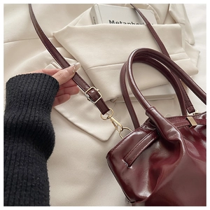 Detailed close-up of dark red glossy leather bag with elegant gold metal buckles