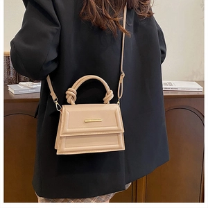 Detail showing the beige leather bag with a unique knotted handle and gold metal bar