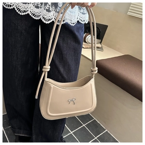 Close-up of beige faux leather shoulder bag featuring a silver metal bow and knotted strap
