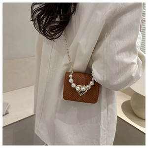 Detail of a brown woven square bag with a pearl handle and heart-shaped metal lock