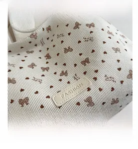 Detail of corduroy tote bag featuring brown heart prints and a sewn leather fashion label