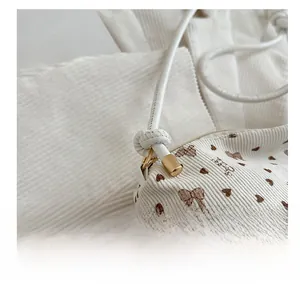 Detail of cream corduroy tote bag featuring brown heart patterns and golden hardware