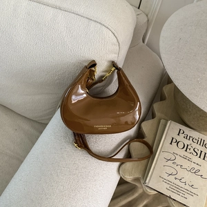 Sac demi-lune en cuir verni marron avec détails dorés sur un canapé blanc texturé