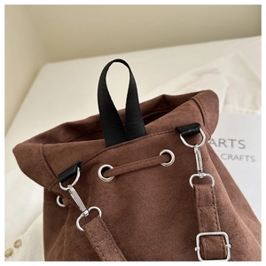 Detail of brown faux suede backpack with drawstring holes, black handle and silver hook