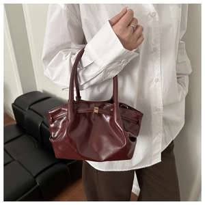 Close-up of wine red glossy patent leather bucket bag with elegant pleats and golden clasp