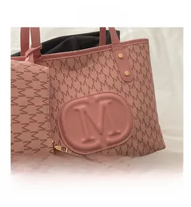 Detail der rosa Tragetasche mit M-Prägung, goldenem Reißverschluss und kleiner Zusatztasche