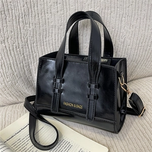 Large black glossy leather tote bag with gold hardware and fashion print on a clean fabric background