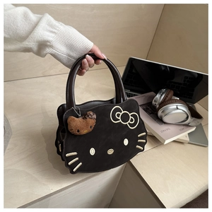 Detail of Hello Kitty embroidered brown suede handbag with plush charm on a wooden desk