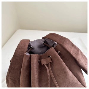 Detail of dark brown suede bucket bag featuring drawstring closure and silver eyelets