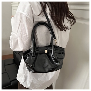Close-up of black glossy cloud bucket bag with gold buckle on a model's shoulder