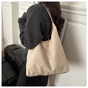 Vista laterale di una borsa a spalla in pelle scamosciata beige opaca indossata da modella