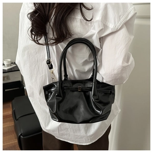 Detail of black glossy pleated bucket bag with gold-tone hardware and top handle
