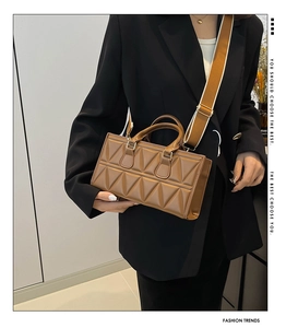 Close-up of caramel brown quilted square bag with wide fabric strap on a model
