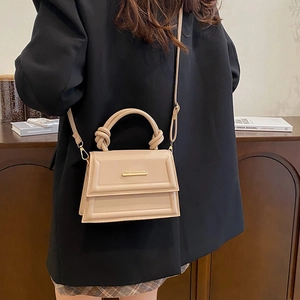 Chic beige crossbody bag with a knot handle and gold buckle worn on a black blazer