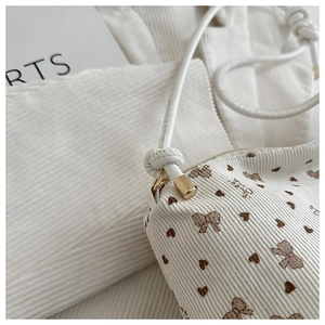 Detail of white corduroy tote bag featuring brown bow prints and fine shoulder strap