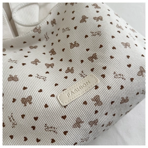 Close-up of white corduroy tote bag featuring brown bow prints and a leather fashion tag