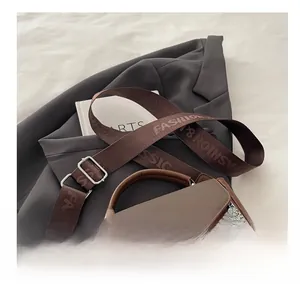 Detail of a brown patchwork crossbody bag with a branded fabric strap on a suit