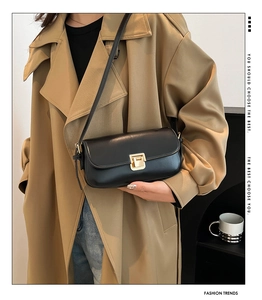 Detail einer schwarzen Satteltasche mit goldener Schnalle zu einem beigen Trenchcoat
