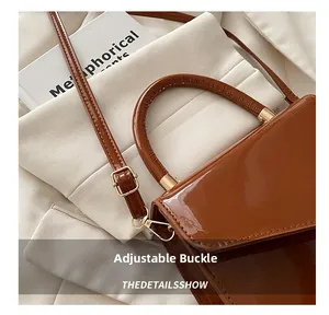 Close-up of brown patent leather handbag with gold metal hardware and adjustable strap buckle