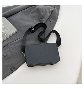 Detail showing litchi grain leather texture and wide nylon strap on black crossbody bag