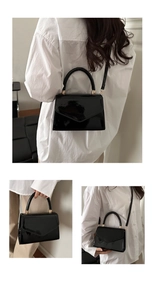 Detail view of black patent leather crossbody bag with top handle and gold hardware