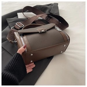 Detail of dark brown patchwork handbag showing mixed fabric textures and metal zippers