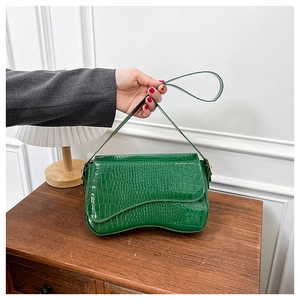 Detail view of green crocodile embossed faux leather shoulder bag on a wooden cabinet