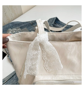 Détail d'un sac cabas blanc brillant avec un nœud en dentelle et une fermeture éclair