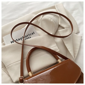 Detail of glossy brown patent leather bag with gold hardware on beige suit