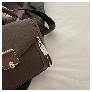 Detail shot of textured dark brown handbag with silver industrial lock and woven strap