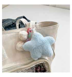 Détail d'une étoile en peluche bleu clair et pompons beiges sur un sac transparent