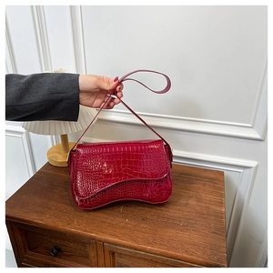 Detail of burgundy crocodile pattern crossbody bag with a wave-shaped bottom design