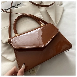 Detail of a brown patent leather crossbody bag with glossy finish and gold-tone hardware
