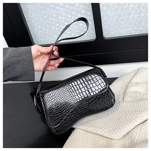 Close-up of black crocodile embossed patent leather handbag with curved crescent bottom