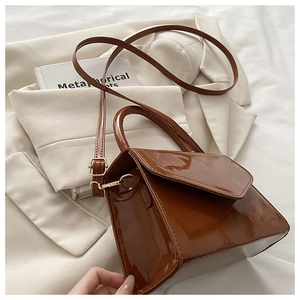 Close-up of brown patent leather crossbody bag on white blazer with golden hardware detail