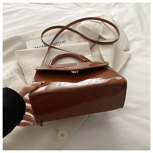Detailed view of brown patent leather handbag with gold buckle on a beige blazer