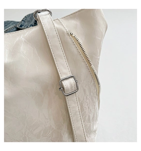 Détails de la boucle argentée et du zip sur le sac à bandoulière crème à texture plissée