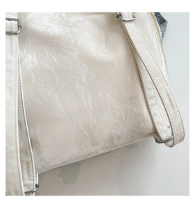 Gros plan du sac plissé blanc avec anneaux en argent et détails zip en denim bleu