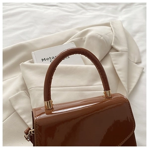 Detail of the glossy brown patent leather texture and gold hardware on the handbag