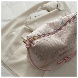 Detail of pink quilted tote bag with colorful embroidery and golden zipper pulls