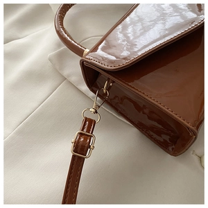 Detail of glossy dark brown patent leather bag showing gold-tone metal hardware and strap