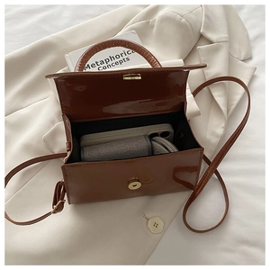 Close-up of brown patent leather mini bag with gold magnetic buckle and interior space