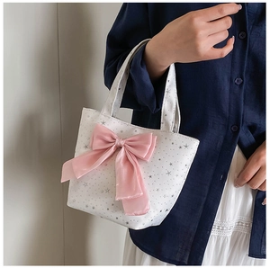 Close-up of a white tote bag featuring a large pink satin bow and silver star patterns