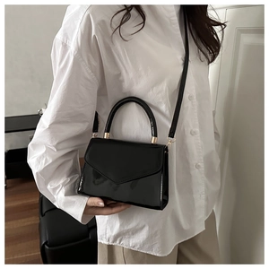Detail of minimalist black patent leather crossbody bag with metallic top handle and gold hardware
