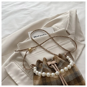 Macro detail of plaid bucket bag with pearl handle and golden chain on beige blazer