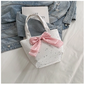 Close-up of a white canvas bucket bag with a pink satin bow and silver stars