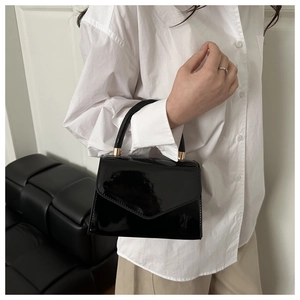 Detail of glossy black patent leather shoulder bag with gold metal hardware and top handle
