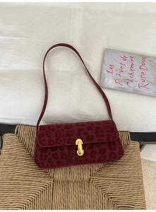 Detail of dark red leopard print shoulder bag with gold clasp on textured surface